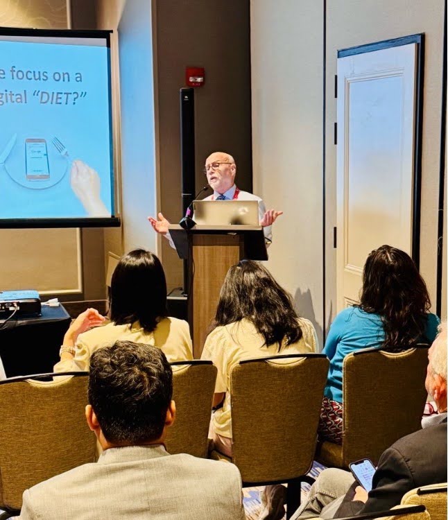 Ronald Yaros speaks at a podium at the AEJMC conference.