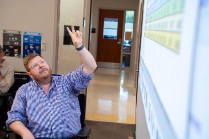 Faculty member Sean Mussenden points to data on a screen while instructing data journalism students in front of a classroom..