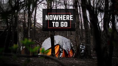 A tent shelter in a wooded area beneath an overpass, with bicycles nearby. A graphic overlay reads “NOWHERE TO GO.”