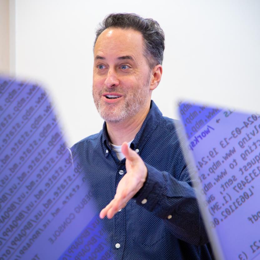 Merrill College's Derek Willis teaching a class, instructing in front of two computers that show data reflected on the screens.