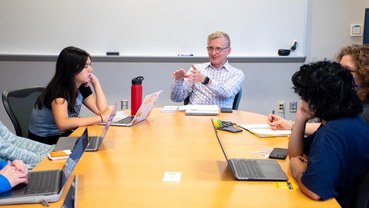 LNN Director Jerry Zremski leads a meeting with several students on computers around a conference table.