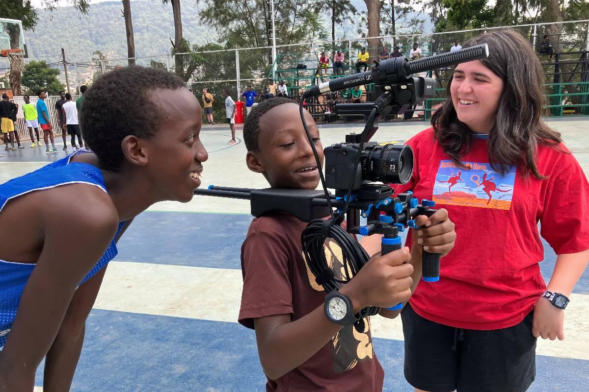Merrill College student shows camera equipment to children on basketball court