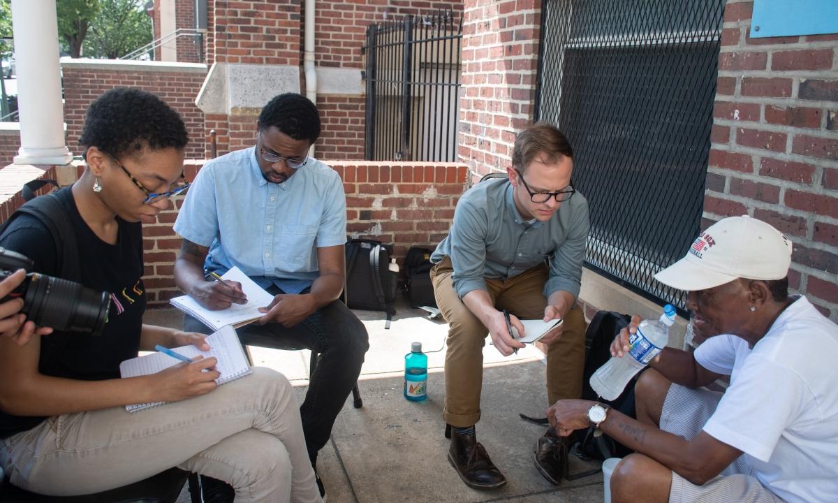 Two men and one woman student interview a source on a brownstone brick porch.