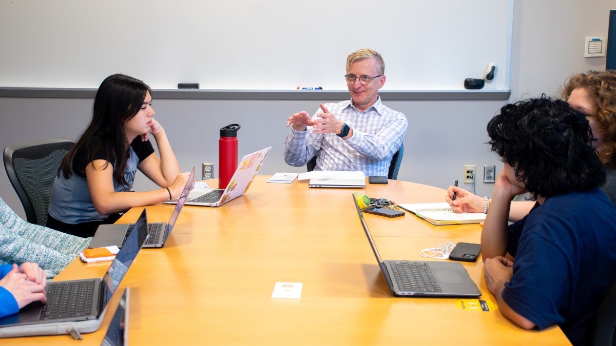 LNN Director Jerry Zremski leads a meeting with several students on computers around a conference table.