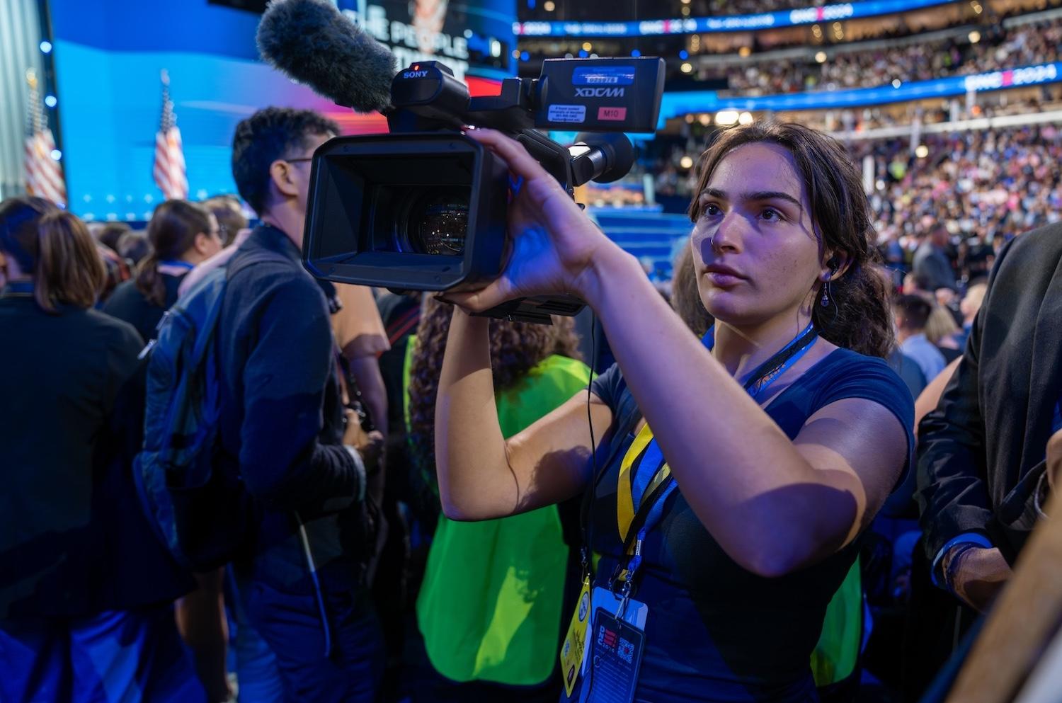 Woman student recording video at a crowded event in an arena
