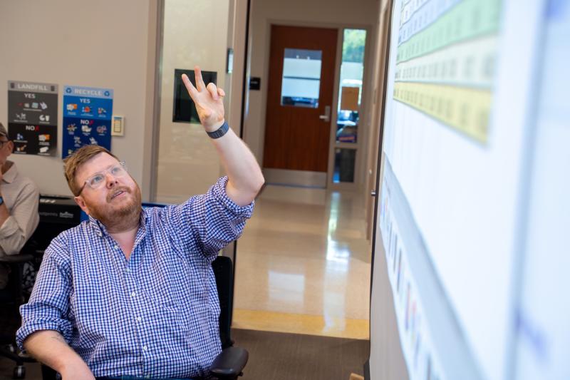Faculty member Sean Mussenden points to data on a screen while instructing data journalism students in front of a classroom..