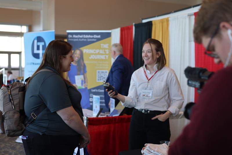 A student journalist interviews an attendee with a portable recorder at an educators' conference.